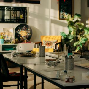 Cozy sunlit studio with tables of art supplies, vibrant plants, and artwork.